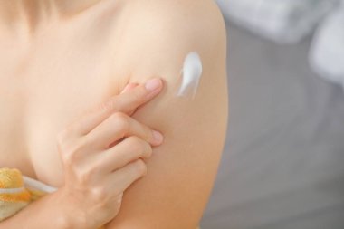 Asyalı kadın yatakta oturuyor ve koluna krem sürüyor..