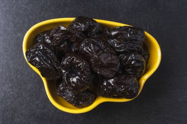 Siyah arka planda sarı bir tabakta tatlı, lezzetli kuru erikler. Lezzetli doğal lezzet, tatlı..