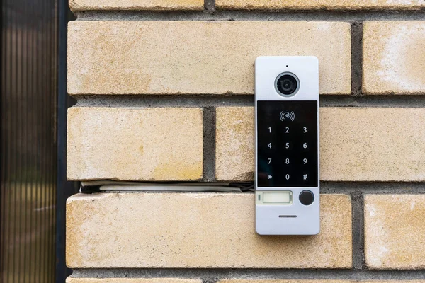 an intercom on the door of a private house, an intercom panel with a video camera on a brick beige fence post of a private house.