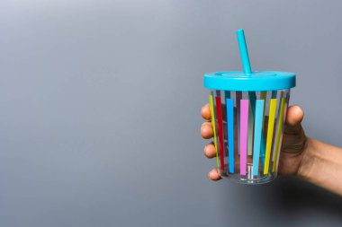 Gri arka planda bir kadının elinde kamış olan renkli bir meyve suyu bardağı, gri arka planda kapağı olan plastik bir bardak, fotokopi alanı, elinde bardak tutan bir kadın.
