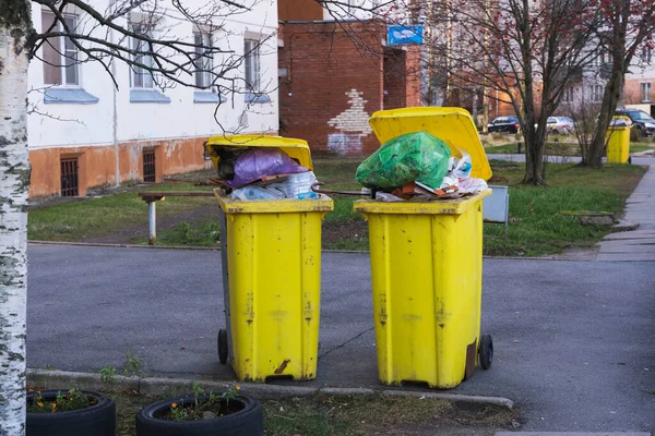 Yellow containers with household garbage in the courtyard of an apartment building, an overflowing garbage can for garbage standing on the sidewalk