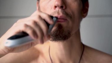 Bir adam sakalını ve bıyığını elektrikli jiletle keser. Tıraş olma zamanı, sakal ve bıyık bakımı, elektrikli traş makinesi.