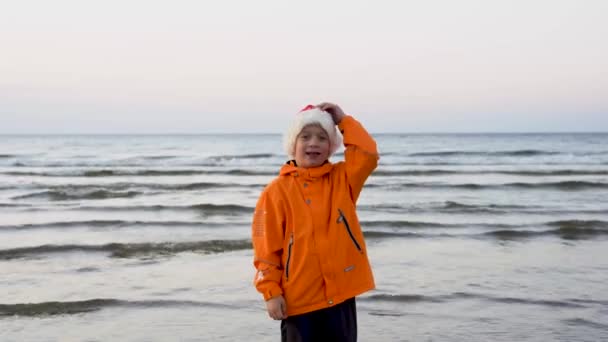 Χαριτωμένο Αγόρι Ένα Καπέλο Χριστούγεννα Χορεύει Χαρούμενα Στην Παραλία Της — Αρχείο Βίντεο