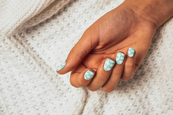 Een mooie vrouwelijke hand met een gekleurde manicure op de achtergrond van een wollen witte gebreide plaid — Stockfoto
