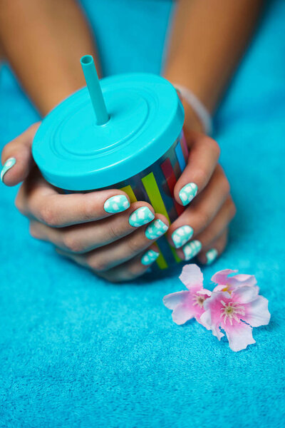 Vertical photo of beautiful womens hands with colored manicure and a multicolored cup with a drinking tube