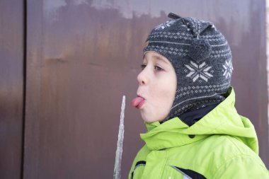 Sevimli anaokulu çocuğu aylaklık ediyor ve uzun buz sarkıtını yalıyor.