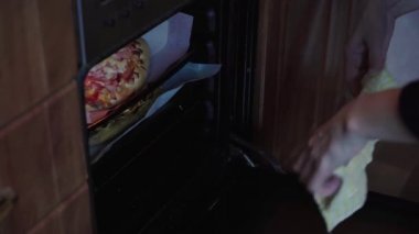 Kadınların elleri fırından fırında pişmiş pizzayı çıkarır.