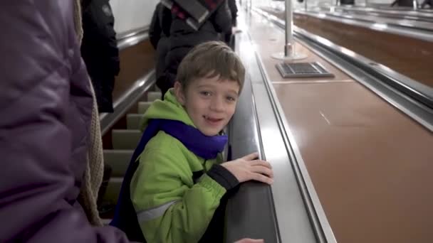 Αστείο αγόρι με χειμωνιάτικα ρούχα ανεβαίνει τις κυλιόμενες σκάλες στο μετρό — Αρχείο Βίντεο