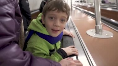 Kışın giyinmiş komik çocuk metroda yürüyen merdivene tırmanıyor.