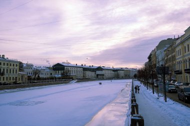 the embankment and the frozen city river in winter and people walk on the ice