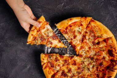 A childs hand takes a piece of delicious pizza on a gray-black background.