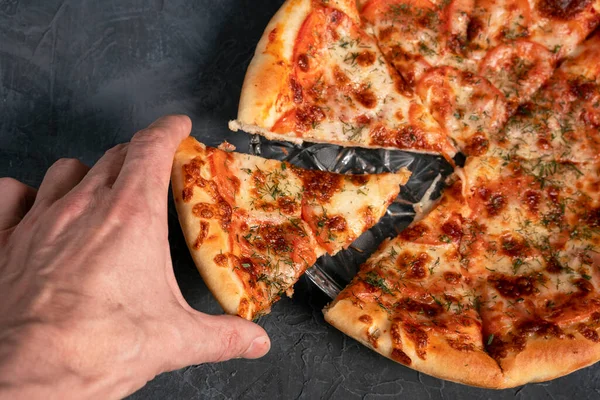 The mans hand takes a piece of delicious pizza on a gray-black background — Stok fotoğraf