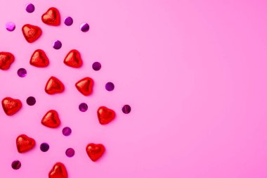 Folyo ve konfetiye sarılmış kalp şeklinde parlak şekerlerle süslü zarif pembe arka plan. Bir kartpostal için güzel bir geçmiş. Sitenin afişi. Boşluğu kopyala