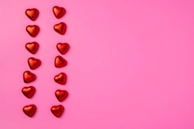 Kupa dereleri, folyoya sarılmış kalp şeklinde parlak şekerlemelerle dolu Parlak Pembe arka plan. Bir kartpostal için güzel bir geçmiş. Sitenin afişi. Boşluğu kopyala