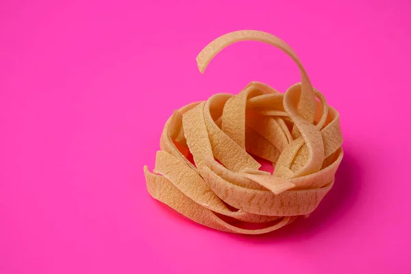 Pembe arka planda çiğ tagliatelle yuvası, makarna yuvası, yumurta ezmesi yuvası, kenar görüş
