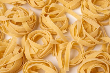 Çiğ tagliatelle, yuva makarnası, yumurta makarnası beyaz arka planda bir desen oluşturulmuş, desen yukarıdan bir yan görünüş.