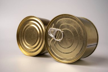Konserve yiyeceklerle dolu iki yuvarlak teneke kutu beyaz bir arka planda konserve yiyeceğin üzerinde yatıyor.