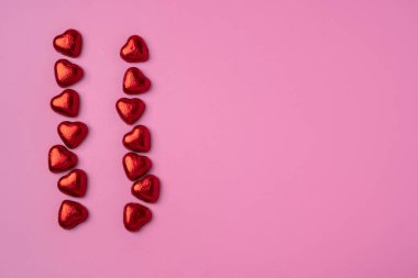 Folyoya sarılmış kalp şeklinde parlak şekerler ile parlak pembe arka planda iki kupa deresi. Bir kartpostal için güzel bir geçmiş. Boşluğu kopyala