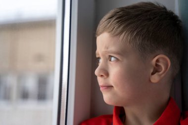 Pencereden dışarı bakıp evde oturan beyaz bir çocuğun portresi.