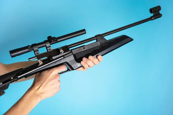 Svart gevär med optisk syn i män händer på en blå bakgrund, vapen — Stockfoto