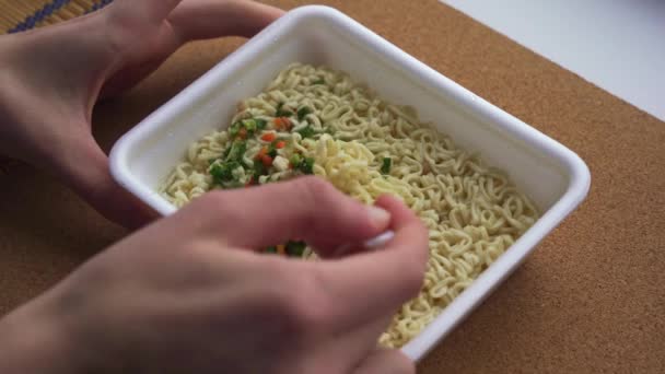 The hands of a teenager mix dried vegetables into Chinese instant noodles. close-up. Slow motion — Stock Video