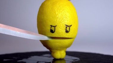 Bir mutfak bıçağı ve ortadan ikiye bölünmüş sarı bir limon stilize edilmiş bir ağız ve boyalı gözler.