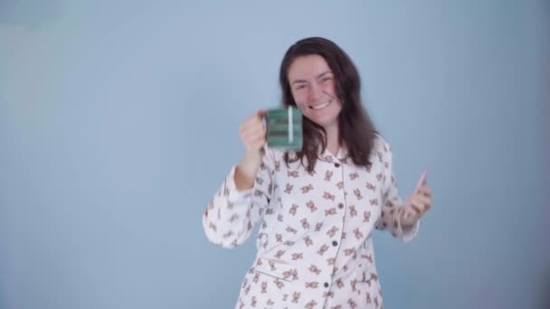 Una mujer caucásica bonita feliz vestida en pijama con una taza de té en sus manos está bailando divertido — Vídeos de Stock