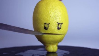 Küçük bir mutfak bıçağı ve ortadan ikiye bölünmüş sarı bir limon stilize edilmiş bir ağız ve boyalı gözler.