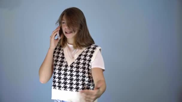 Tini lány beszél izgatottan a telefon kék háttér — Stock videók