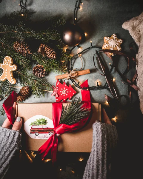 Noel hediyesi hazırlayan kadın elleri. Noel 'le ilgili nesnelerden oluşan yaratıcı bir düzen. Üst manzara, düz yatış. En düşük mevsim ve tatil konsepti.