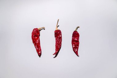 Gri arka planda üç kırmızı biberden oluşan yaratıcı bir düzen. Üst manzara, düz yatış. En az besin ve mevsime özel konsept.