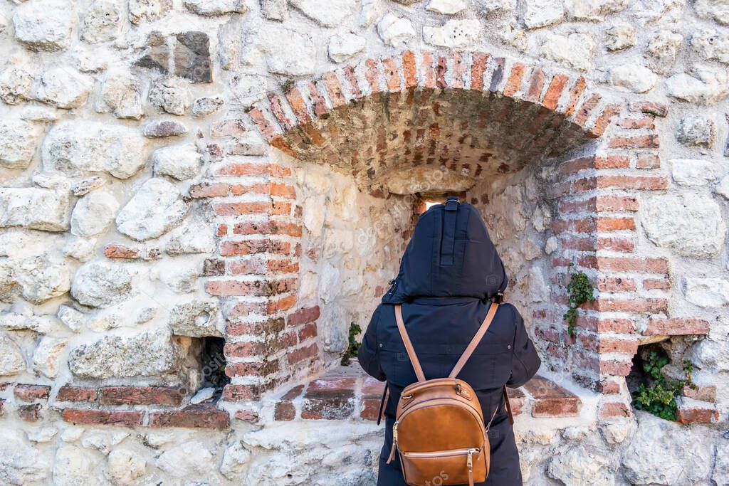 Girl from behind with hooded vest, facing a medieval ancient wall