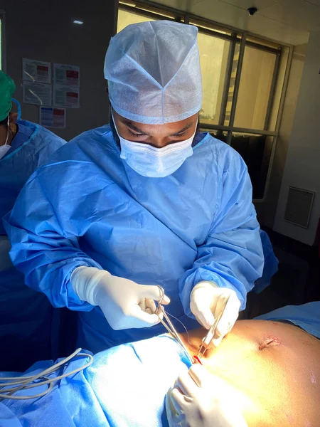 A picture of a Indian doctor doing suturing after the surgery in an operation theater