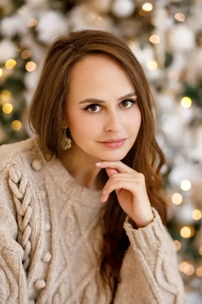 身穿米色针织保暖毛衣和蓝色牛仔裤的年轻女子 背景是圣诞装饰品 — 图库照片