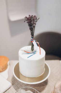 Masanın arka planında lavanta filizi ile süslenmiş, beyaz mastikli lavantalı kek.