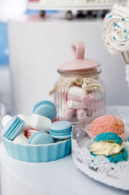 Mavi badem kurabiyesi, beyaz marşmelov ve masanın üzerinde pembe kapaklı bir kavanozun arka planına karşı çok renkli kekler.