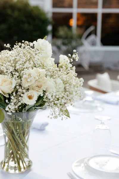 白色桌布上的桌子上有一束白玫瑰和吉普赛葡萄酒 背景上有餐具 — 图库照片