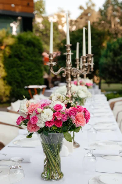 一束白色的玫瑰 粉红色的玫瑰 节庆桌上的粉色康乃馨 菜盘上装饰着大烛台 背景是绿色的花园 — 图库照片