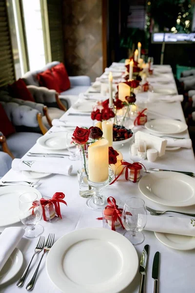 餐桌上摆满盘子 餐具和餐巾 用栗色盒子 蜡烛和红玫瑰瓶装饰的餐桌 — 图库照片