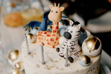 Hayvan heykelcikleri, zebra ve zürafa ile süslenmiş doğum günü pastası, mumlar ve altın balonlar