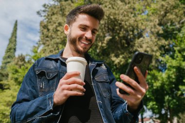 Gülümseyen genç bir adam, elinde kahve fincanı olan yakışıklı bir adam. Video görüşmesi yapıyor, ekranda gülümsüyor.