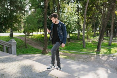 Merdivenler, merdivenleri çıkan genç adam telefonuna bakıyor, rahat giyinen adam güzel havanın, parkın ve baharın tadını çıkarıyor.