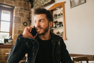 Telefon, eski bir kafede konuşan genç yakışıklı adam, ahşap tonlar ve estetik mekan, iyi ve eğlenceli zaman geçirin.