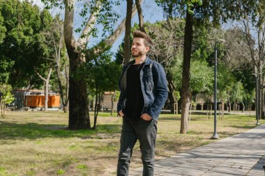 Kot pantolonlu genç adam parkta güzel bir günde ağaçların arasında yavaşça yürüyor. Doğada yalnız zaman geçirmek. Huzurlu atmosfer.