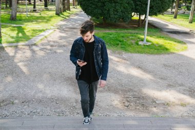 Merdivenler, merdivenleri çıkan genç adam telefonuna bakıyor, rahat giyinen adam güzel havanın, parkın ve baharın tadını çıkarıyor.