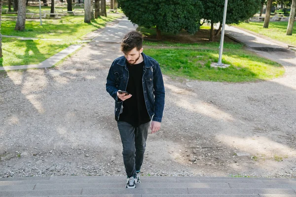 Merdivenler, merdivenleri çıkan genç adam telefonuna bakıyor, rahat giyinen adam güzel havanın, parkın ve baharın tadını çıkarıyor.