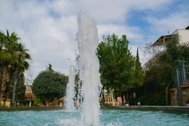 Su havuzu, havuzdan fışkıran çeşme ve arka planda mavi bulutlu bir gökyüzü, halk parkı ve doğa.