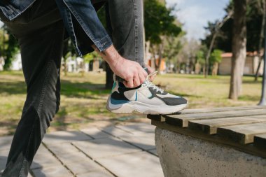 Kot ceket giyen genç adam yürüyüş yapan adam ayağa kalkıp ayakkabı bağcığı deniyor koşuya hazırlanıyor ve dışarıda yürüyor sokak sağlık parkı, sağlıklı egzersiz konsepti.