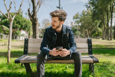 Kot pantolon giymiş genç bir adam elinde bir telefonla başka tarafa bakıyor. Kız arkadaşını düşünen yalnız bir adam. Bir bankta rahatça oturup başka tarafa bakmak..