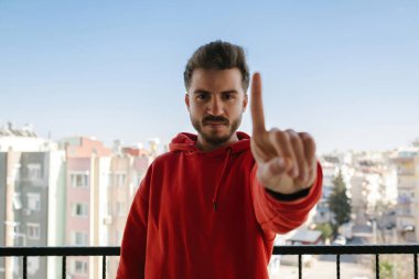 El işareti, balkondaki genç adam parmaklarıyla bir işaret yapıyor, kızgın bir bakış ve yüz ifadesi.